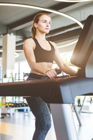 The athletic woman dressed in a black sportswear running on the treadmill in the modern gym