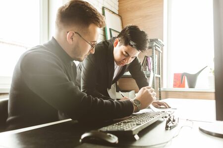 Young office worker sitting at desk, using computer. Two business man talking