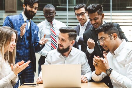 A team of young office workers, businessmen with laptop working at the table, communicating together...