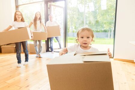 Happy young family, parents daughter and son, unpacking boxes and moving into a new home. funny kids run in with boxesの写真素材