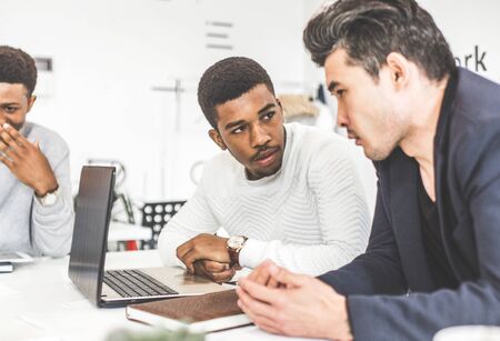 A team of young office workers, businessmen with laptop working at the table, communicating together in an office. Corporate businessteam and manager in a meeting. coworking.の写真素材