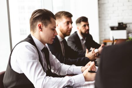 A team of young businessmen in suits working and communicating together in an office. Corporate...
