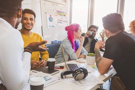 Group of multi ethnic executives discussing during a meeting. Business man and woman sitting around table at office and smiling. A team of young creative designersの写真素材
