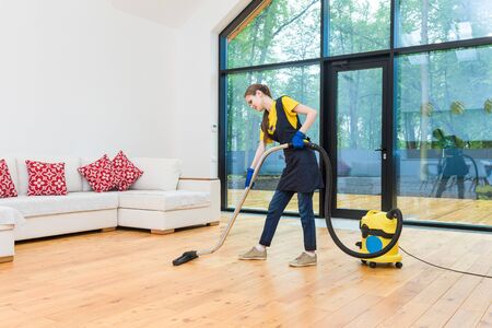 professional cleaning service. woman in uniform and gloves does the cleaning in a cottage. the worker vacuums the floor with professional equipment.の写真素材