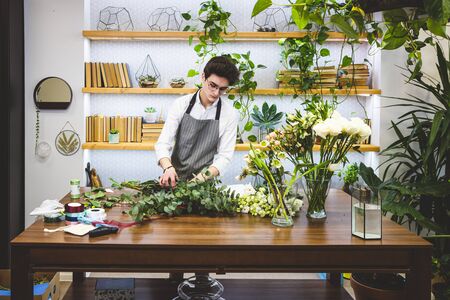 Attractive young male florist with glasses and apron works in a flower shop.の写真素材