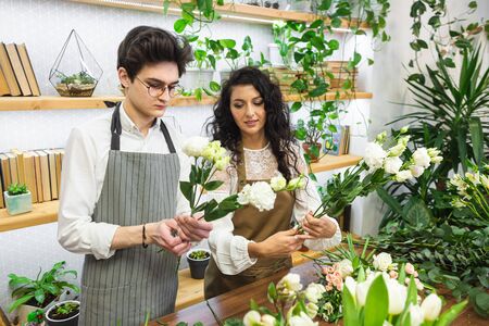 Attractive experienced female florist teaches a young man how to work in a flower shopの写真素材