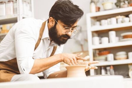 A young male potter is engaged in crafA young male potter is engaged in craft in his workshop on a potter's wheel and makes a clay product.の写真素材