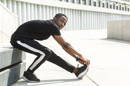 Athletic young afroamerican runner doing warm up on the promenade. Black Male running on outdoors....