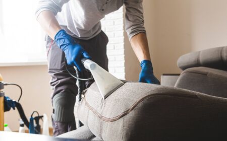 Dry cleaners man employee removing dirt from furniture in flat, closeup, vacuum clean sofa with professional equipmentの写真素材