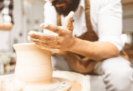 A young male potter works in his workshop on a potter's wheel and makes clay products. Close-up of...
