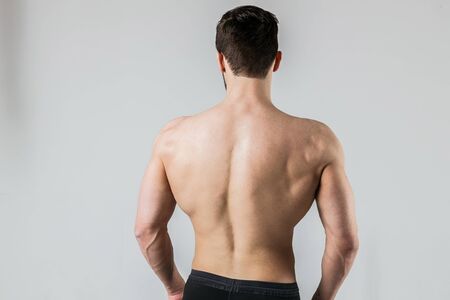Back of a muscular bodybuilder athlete posing on a light background.の写真素材