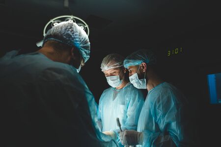 An international professional team of surgeon, assistants and anesthesiologist perform a complex operation on a patient under general anesthesia. Dark atmospheric photography theme in low key.の写真素材