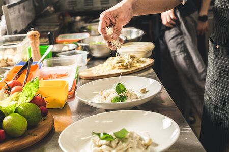 Professional chef cooking in the kitchen restaurant at the hotel, preparing dinner. A cook in an apron makes a salad of vegetables and pizza.の写真素材