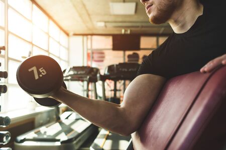 Close-up of a muscular man performs exercises in the gym. Strength training with dumbbellsの写真素材