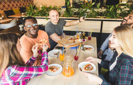 A company of multicultural young people in a cafe eating pizza, drinking cocktails, having funの写真素材