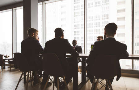 Silhouettes of people sitting at the table. A team of young businessmen working and communicating together in an office. Corporate businessteam and manager in a meeting.の写真素材