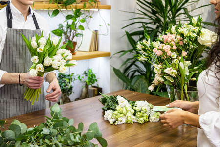 Shopping at the store. Attractive male seller sells a bouquet of flowers in a flower shop and receives moneyの写真素材