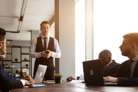 A team of young businessmen in suits working and communicating together in an office. Corporate...