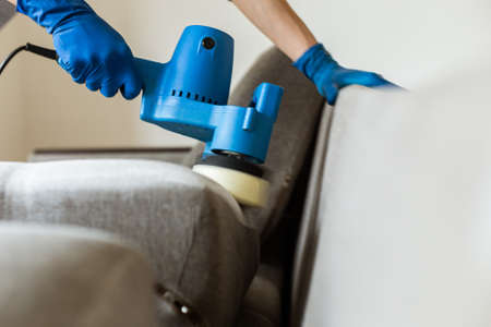 Dry cleaners man employee removing dirt from furniture in flat, closeup, vacuum clean sofa with professional equipment. cleaning service.の写真素材