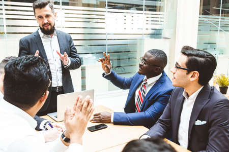 A team of young office workers, businessmen with laptop working at the table, communicating together...