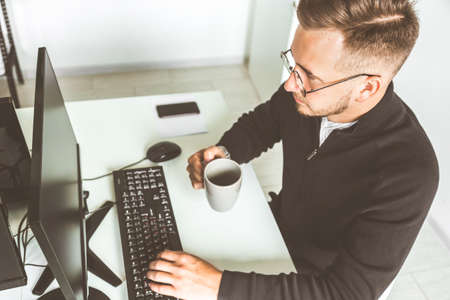 Young office worker sitting at desk, using computer. Two business man talking.の写真素材