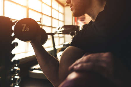 Young male athlete performs exercises with dumbbells in the gym. Strength training.の写真素材