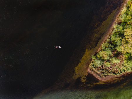 An overhead view of a motor boat sails against the current on a colored blue-green river. Aerial drone shootingの写真素材