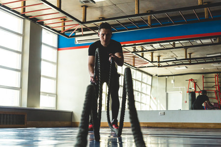 Portrait shot of strong young man training with battle ropes in the exercise gymの写真素材