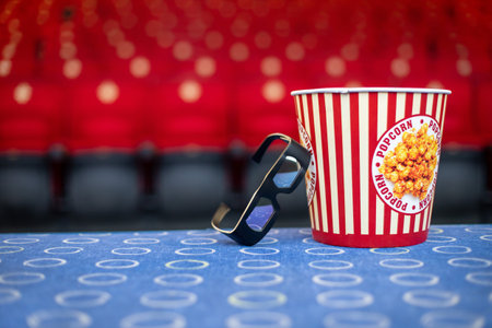 A large bucket of popcorn and 3D glasses on the background of cinema chairs