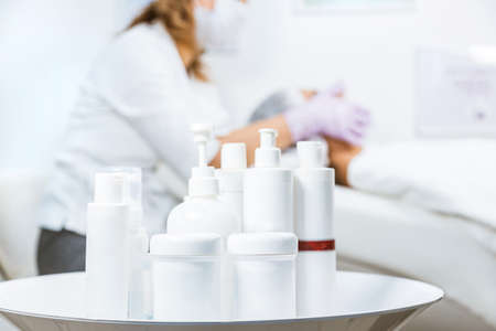 A set of cans and containers of skin care products in the foreground and a specialist beautician with a woman at the reception in the background. Mockupの写真素材