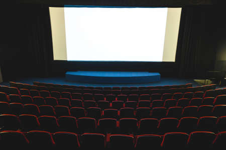 Cinema interior. Chairs in a large empty cinema hall against a white projection screenの写真素材