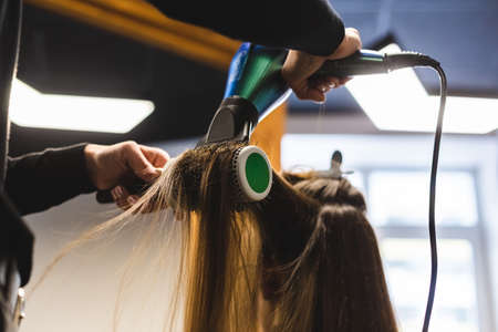 Master woman hairdresser dries the girls hair with a hairdryer and combs after washing in the beauty salon.の写真素材