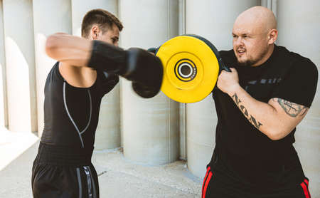 Two men exercising and fighting in outside. Boxer in gloves is training with a coach