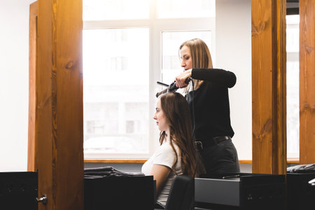 Master woman hairdresser gently curls hair curling girl in a beauty salon. Hair styling
