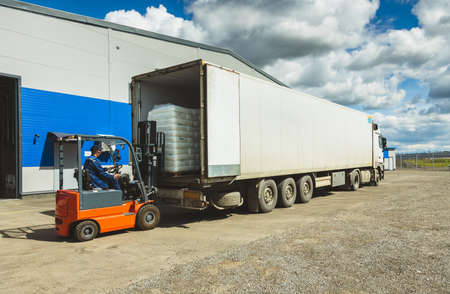 A man on a forklift works in a large warehouse, unloads bags of raw materials into a truck for...