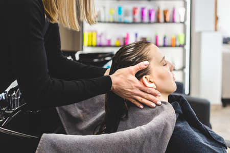 Master woman hairdresser gently washes the girls hair with shampoo and conditioner before styling in...