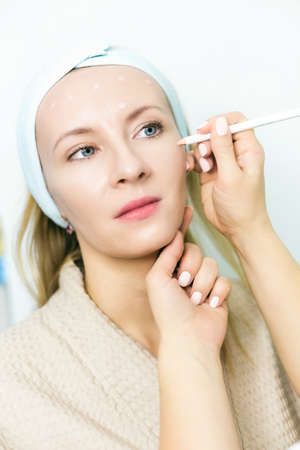 Skin care and facelift. A young woman at a beauticians appointment. A specialist examines it and makes markings with a special pencilの写真素材