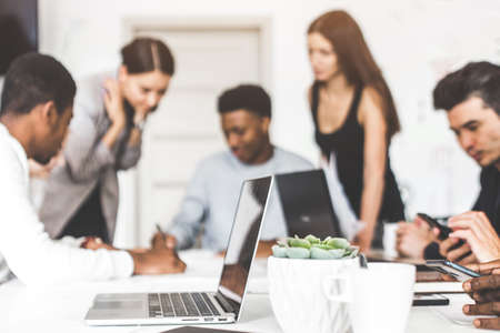 A team of young office workers, businessmen with laptop working at the table, communicating together...