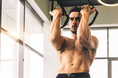 Handsome young sporty male bodybuilder with naked torso doing exercises in the gym