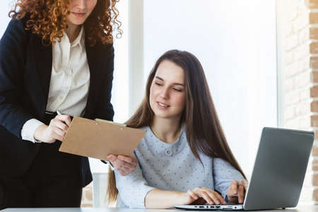 Two beautiful young woman talking and discussing working moments with laptop in the office.