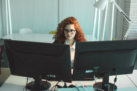 Portrait of a beautiful young business woman with red curly hair taking glass. The girl reads a book in the office. Successful career and leisure time and hobbiesの写真素材