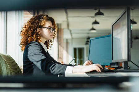 Portrait of a beautiful young business woman with red curly hair working productively in the office....