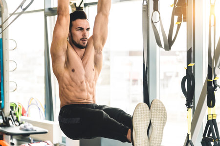 Handsome young sporty male bodybuilder with naked torso doing exercises in the gym