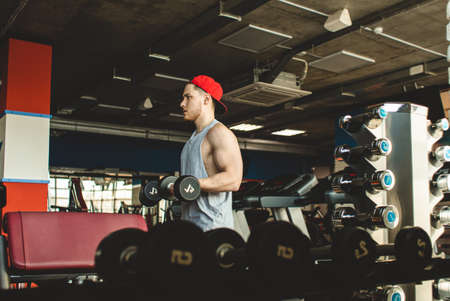 Portrait of a muscular man performs exercises in the gym. Strength training with dumbbells