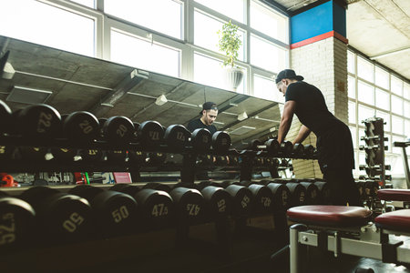 Portrait of an athletic man is training with dumbbells in the gym in front of a mirror.の写真素材