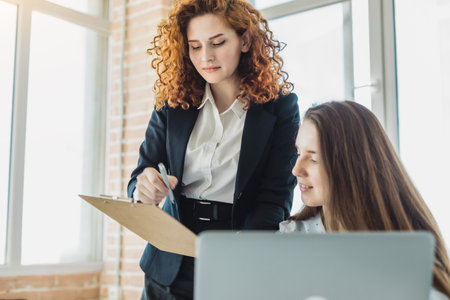 Two beautiful young woman talking and discussing working moments with laptop in the office.の写真素材