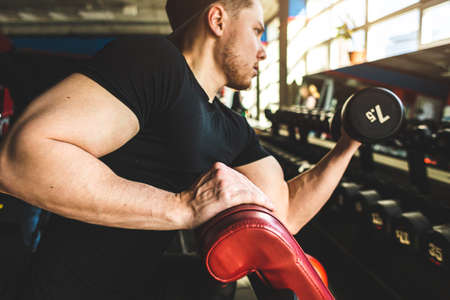 Close-up of a muscular man performs exercises in the gym. Strength training with dumbbellsの写真素材