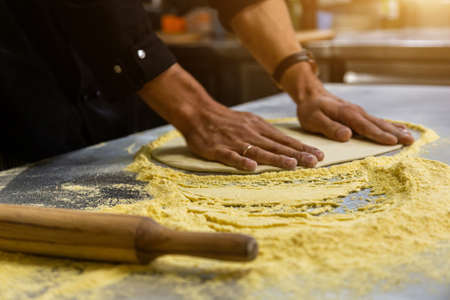 Professional chef cooking in the kitchen restaurant at the hotel, preparing dinner. A cook in an apron makes a pizza. man rolls out pizza doughの写真素材