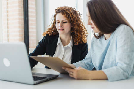 Two beautiful young woman talking and discussing working moments with laptop in the office. staff...