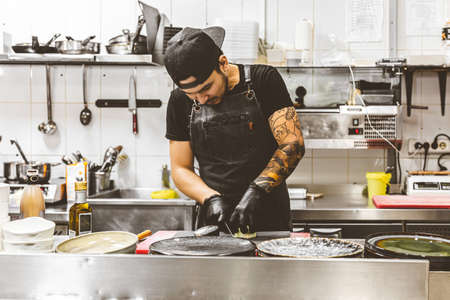 Professional chef cooking in the kitchen restaurant at the hotel, preparing dinner. A cook in an apron makes a salad of vegetables and pizza.の写真素材